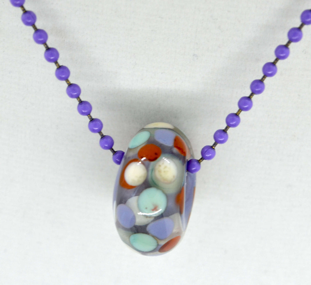 Purple core with orange, purple and light blue encased in clear glass bead on ball chain